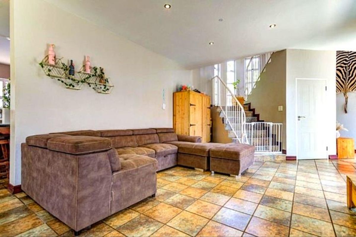 Spacious living area featuring tiled flooring, recessed ceiling lighting, and an open staircase with a metal balustrade.