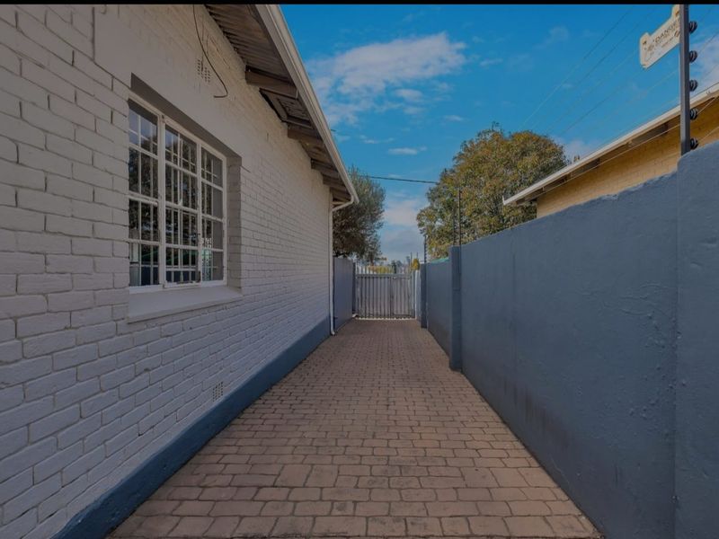 A paved side walkway featuring painted brick walls, secure boundary fencing, and a metal gate leading to the rear of the property.
