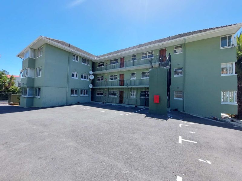 Exterior view of a multi-story apartment complex featuring an asphalt parking area, external stairwell access, and balcony walkways.