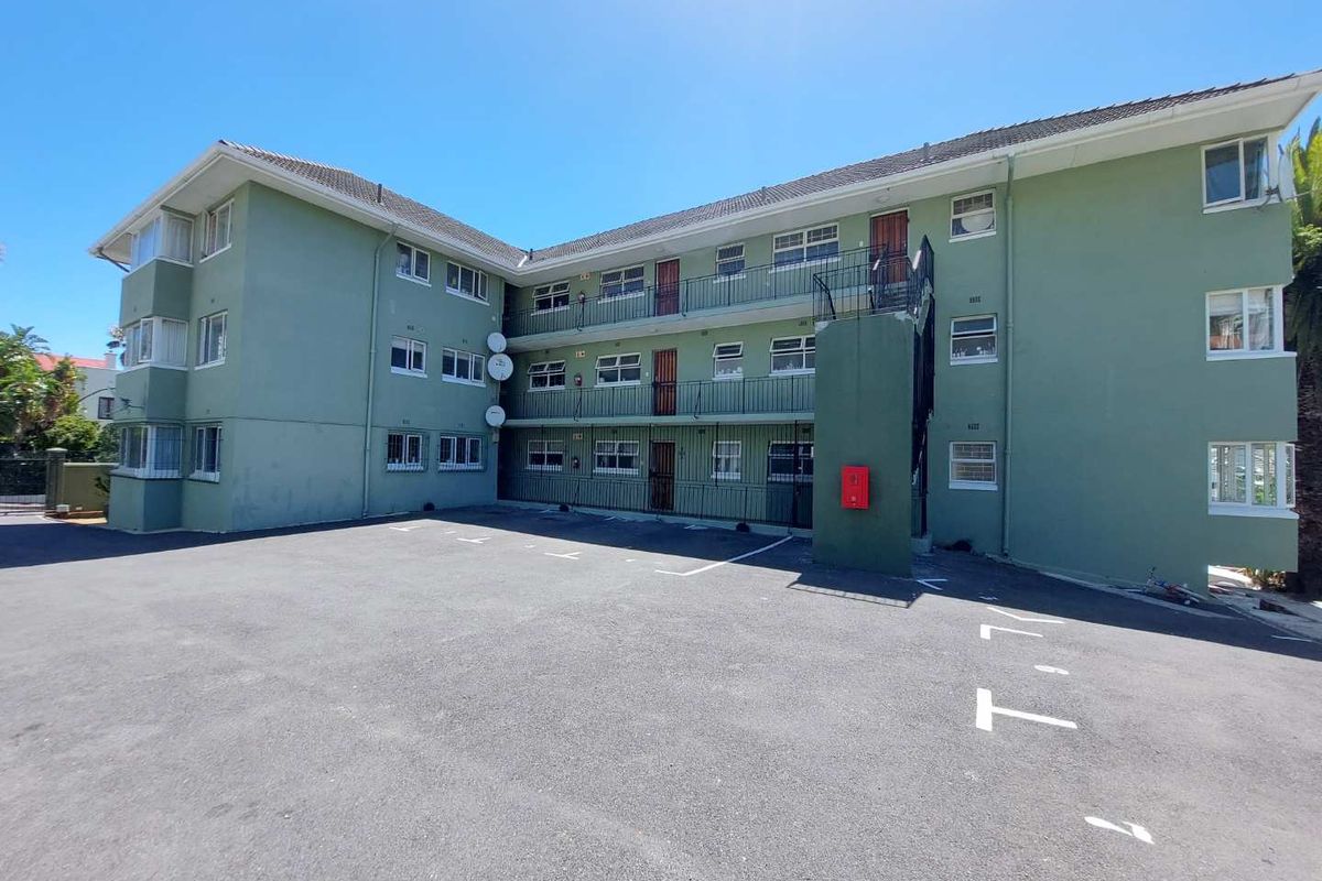 Exterior view of a multi-story apartment complex featuring an asphalt parking area, external stairwell access, and balcony walkways.