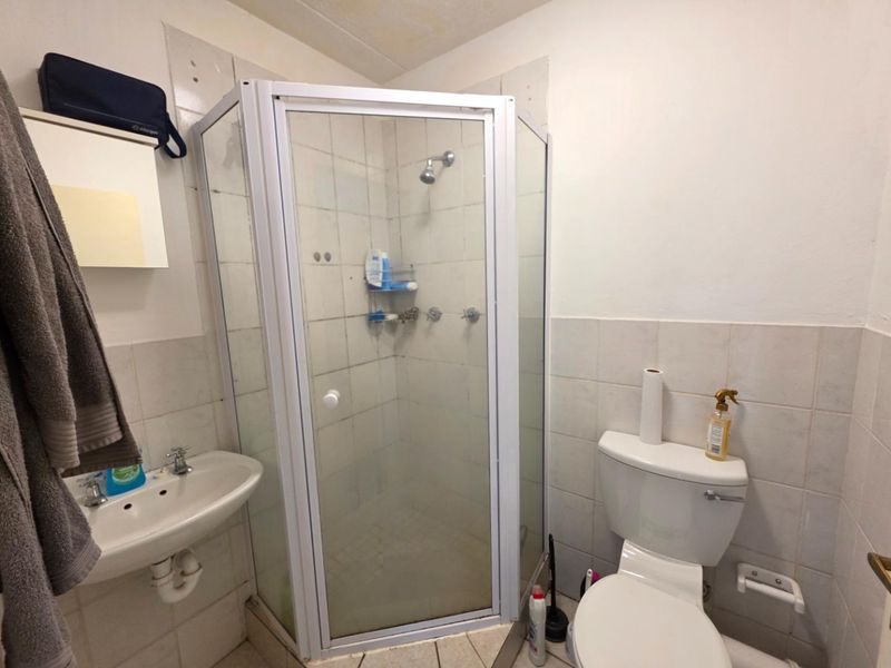 A compact bathroom featuring a corner shower enclosure, wall-mounted basin, and toilet, with tiled finishes throughout.