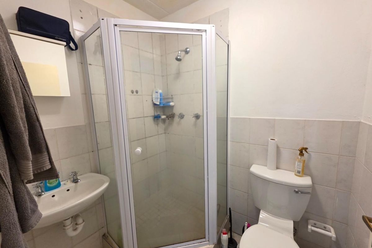 A compact bathroom featuring a corner shower enclosure, wall-mounted basin, and toilet, with tiled finishes throughout.