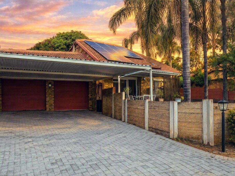 Front view of the townhouse featuring a paved driveway, double garage with carport, and solar panels installed on the tiled roof.