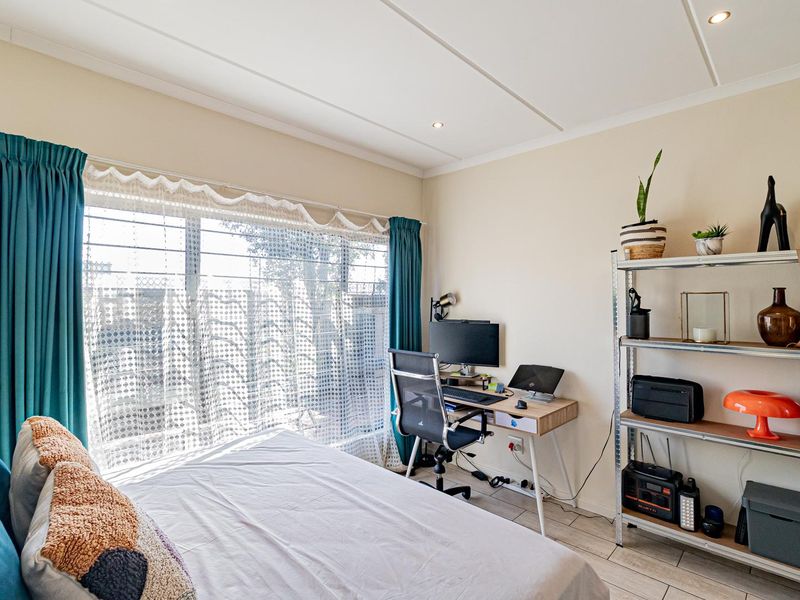 A well-lit bedroom featuring tiled flooring, recessed ceiling lighting, and a large window fitted with security bars.