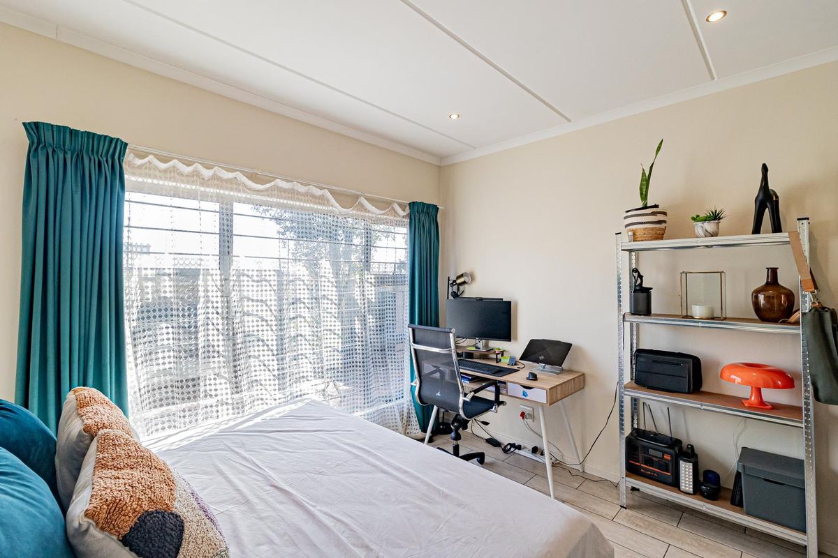A well-lit bedroom featuring tiled flooring, recessed ceiling lighting, and a large window fitted with security bars.