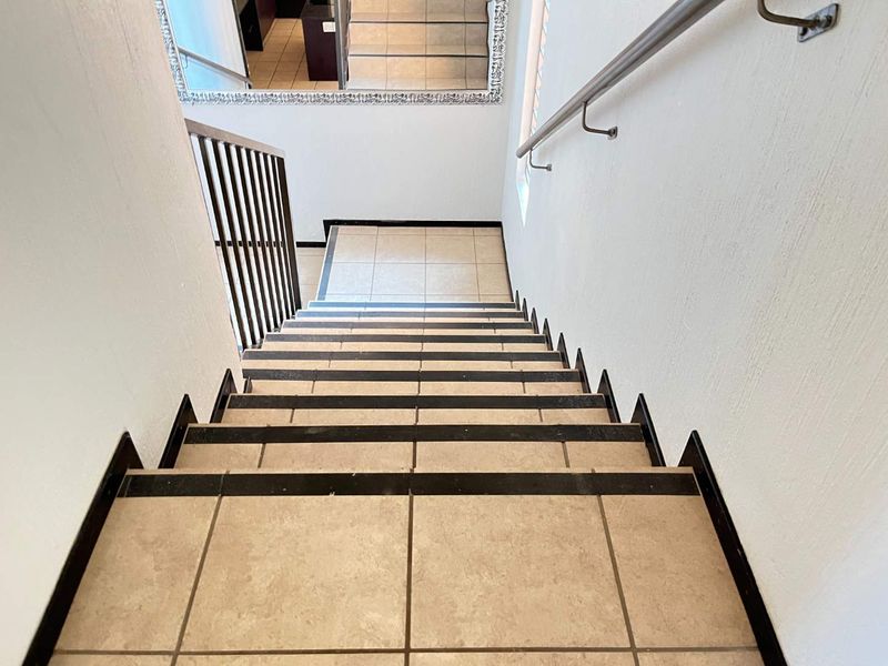 A clean, tiled staircase featuring a metal handrail and balustrade, providing a functional and well-maintained transition between levels.
