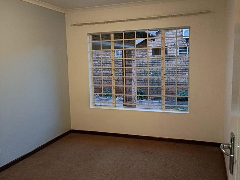 A vacant bedroom featuring carpeted flooring, a flush mount ceiling light, and a window fitted with security bars.