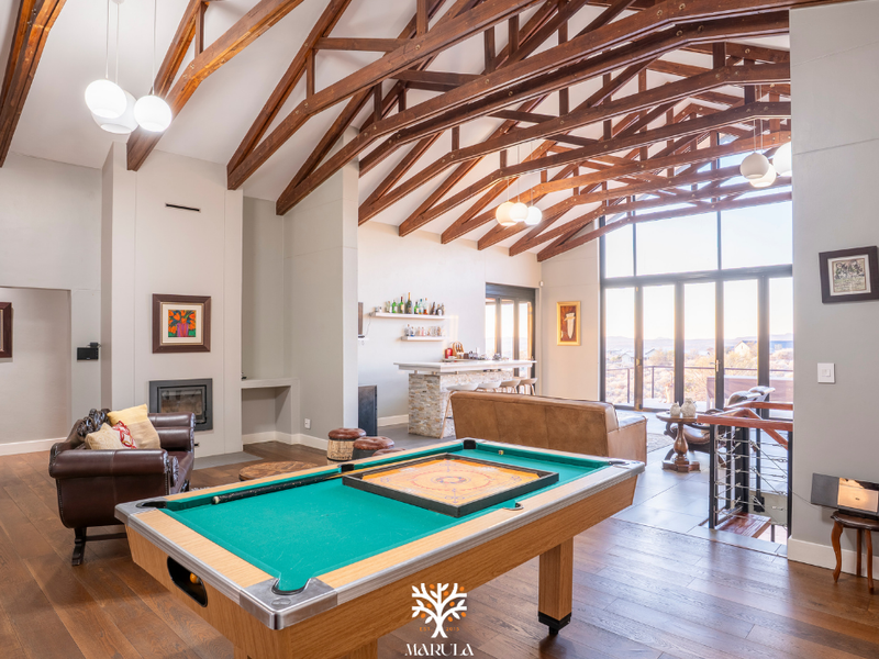 Spacious living area featuring high vaulted ceilings with exposed timber trusses, a built-in fireplace, a custom bar, and expansive glass doors leading outdoors.