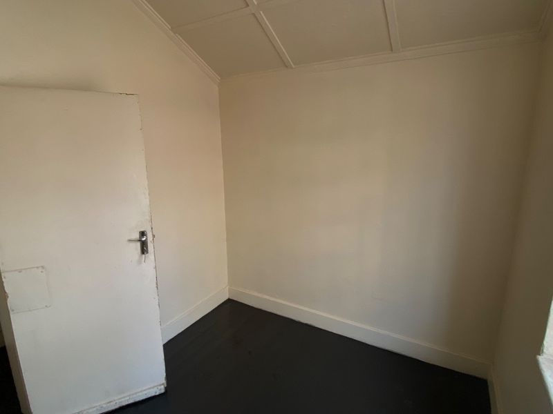 An empty bedroom featuring dark timber flooring, a panelled ceiling, and a window fitted with security bars.