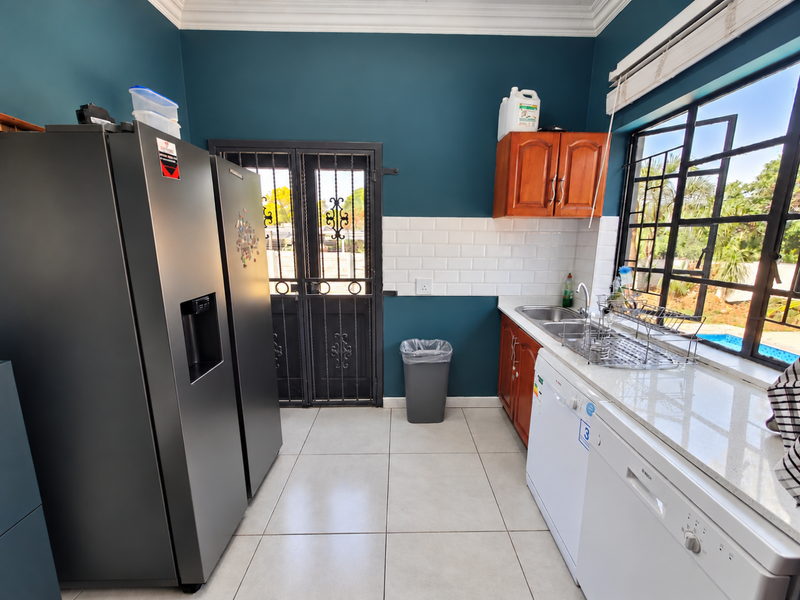 Functional scullery featuring stone countertops, subway tile backsplash, stainless steel sink, and direct access to the exterior via a security gate.