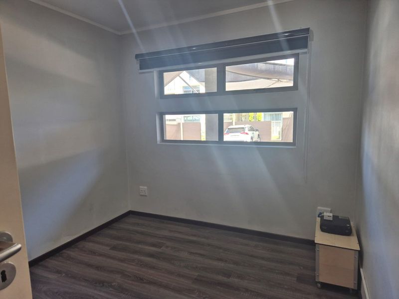 A vacant bedroom featuring dark laminate flooring, neutral walls, and horizontal windows with a fitted roller blind.
