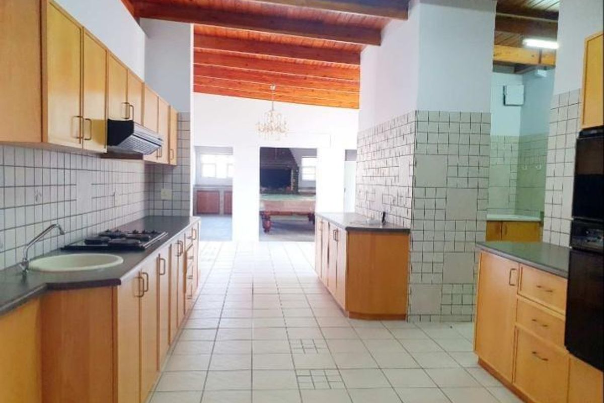 Spacious kitchen featuring wooden cabinetry, built-in hob, extractor fan, and tiled flooring, with an open-plan layout leading to an adjacent living area.