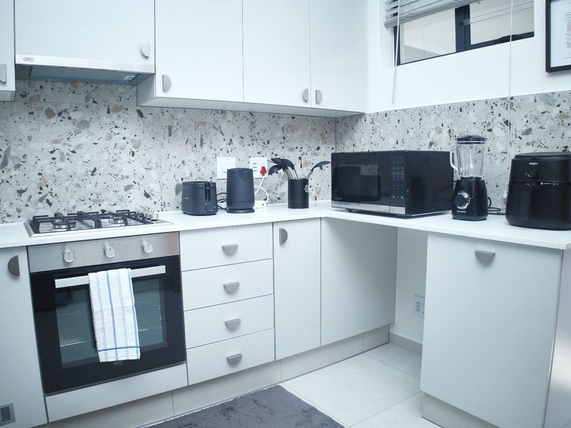 Modern kitchen featuring white cabinetry, quartz countertops, a stylish terrazzo-style backsplash, and integrated gas hob with electric oven.