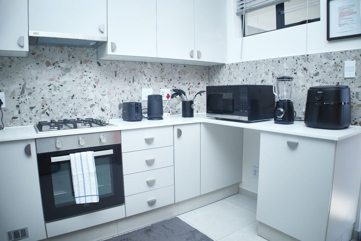 Modern kitchen featuring white cabinetry, quartz countertops, a stylish terrazzo-style backsplash, and integrated gas hob with electric oven.