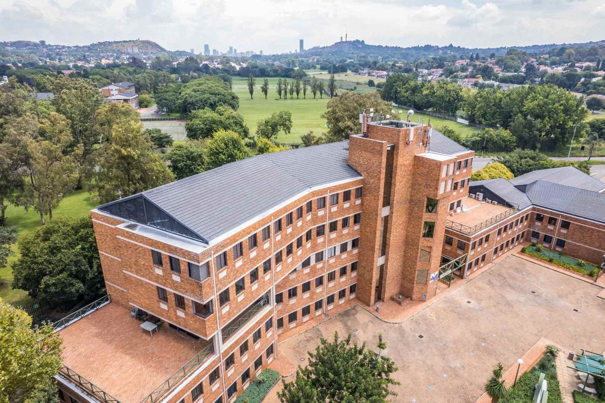 Aerial view of a multi-story brick commercial building featuring a paved courtyard and surrounding landscaped grounds with city skyline views.