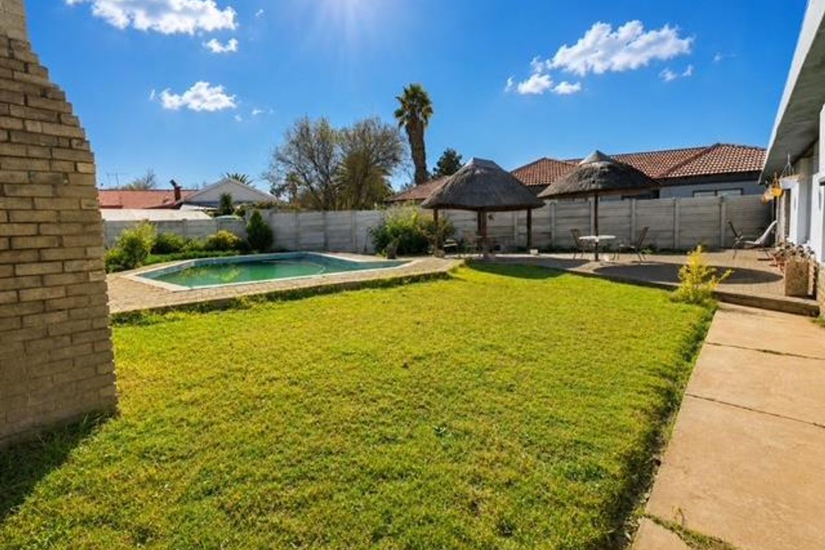 Rear garden featuring a swimming pool, paved patio area, and a traditional thatched lapa, enclosed by a precast concrete boundary wall.