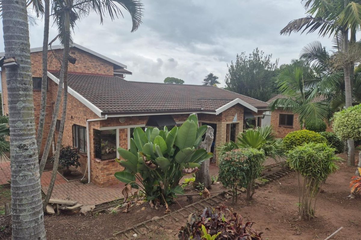 Rear view of a brick house featuring a tiled roof and paved patio area set within a mature garden.