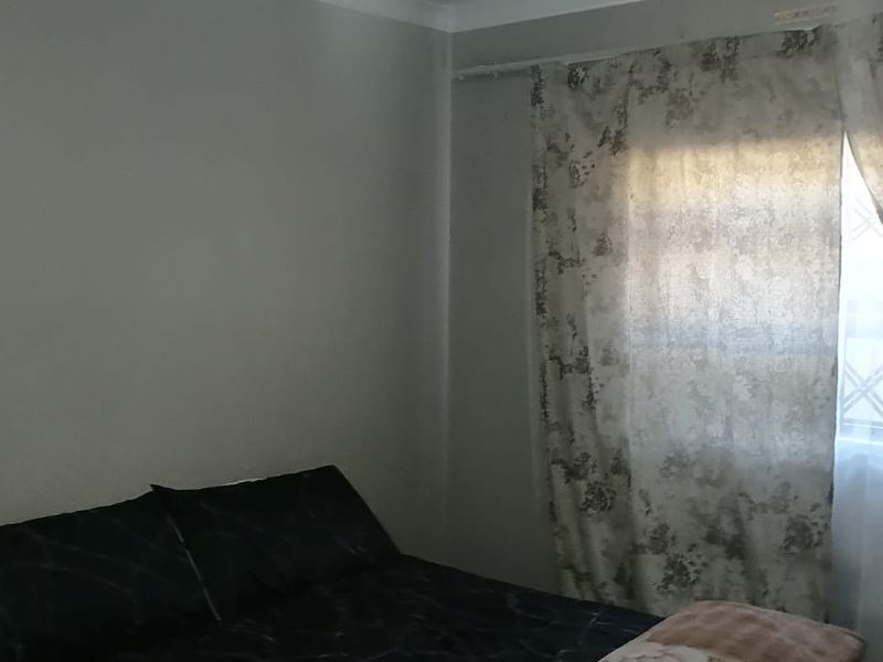 A standard bedroom featuring neutral wall finishes and a window fitted with security bars and curtains.