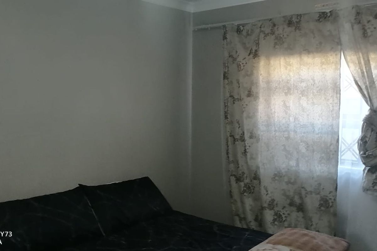 A standard bedroom featuring neutral wall finishes and a window fitted with security bars and curtains.