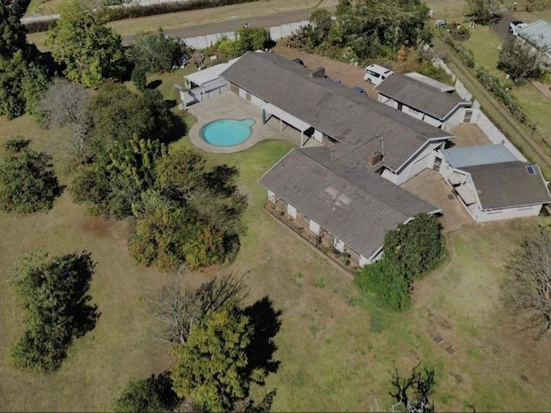 Aerial view of a residential property featuring a large garden, swimming pool, multiple outbuildings, and a tiled roof structure.