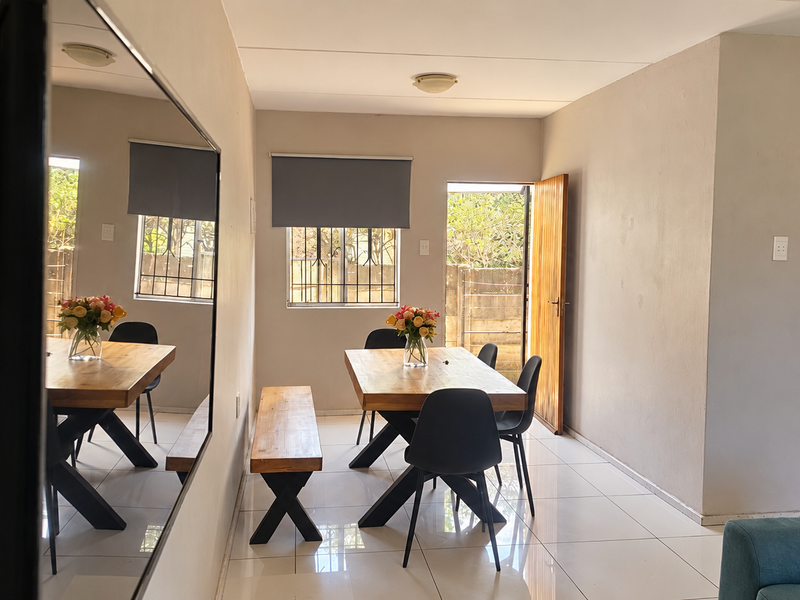 Open-plan living and dining area featuring tiled floors, roller blinds, and a functional kitchen with built-in oven and hob, leading to an outdoor space.