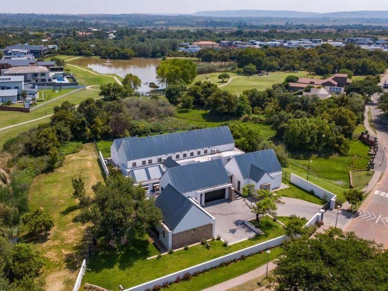 Aerial view of a modern residential property featuring a metal roof, paved driveway, and surrounding landscaped grounds in a scenic estate setting.