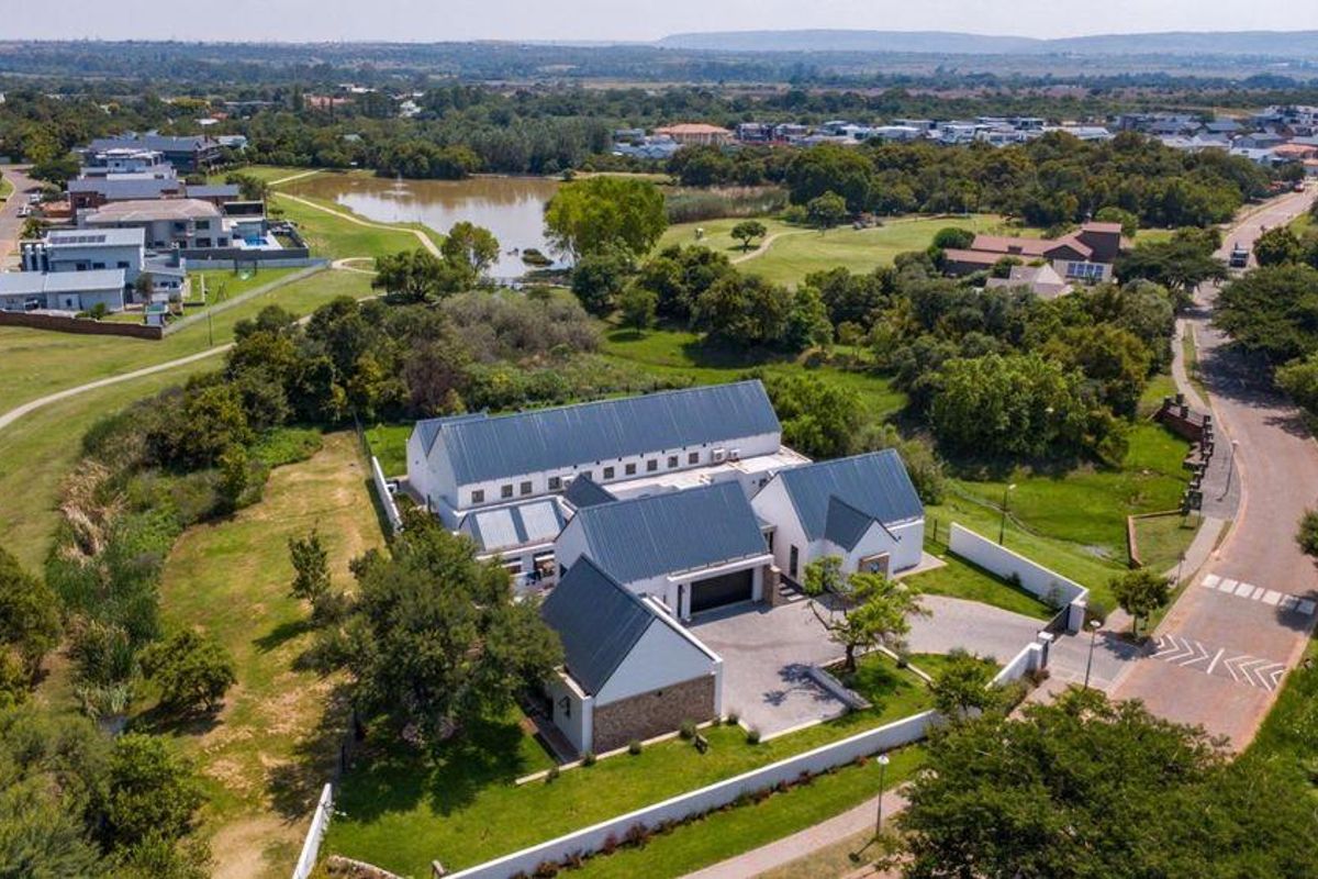 Aerial view of a modern residential property featuring a metal roof, paved driveway, and surrounding landscaped grounds in a scenic estate setting.