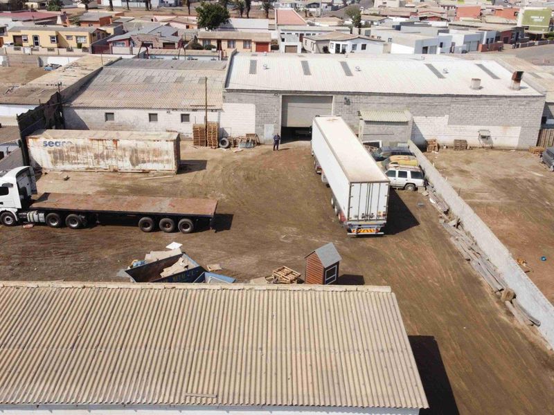Aerial view of a commercial property featuring a large warehouse building with corrugated roofing, concrete block walls, and a spacious unpaved yard area.