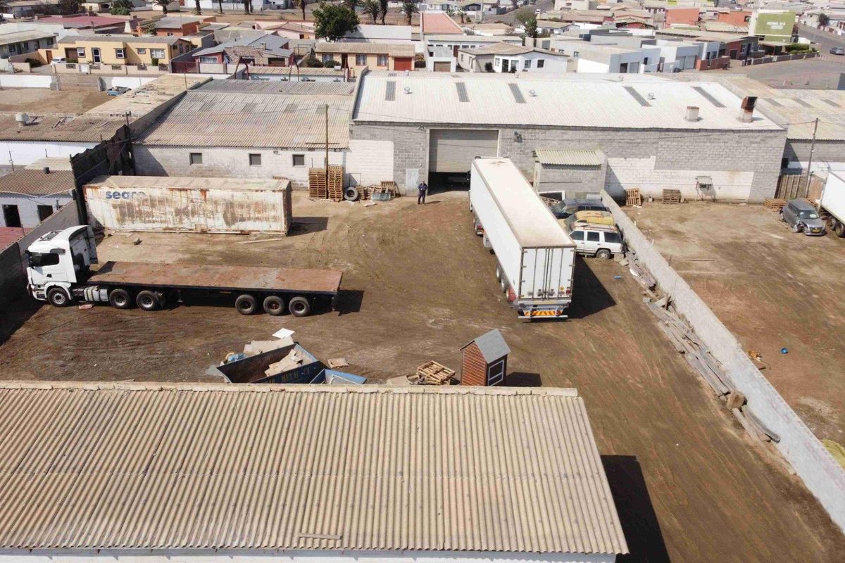 Aerial view of a commercial property featuring a large warehouse building with corrugated roofing, concrete block walls, and a spacious unpaved yard area.