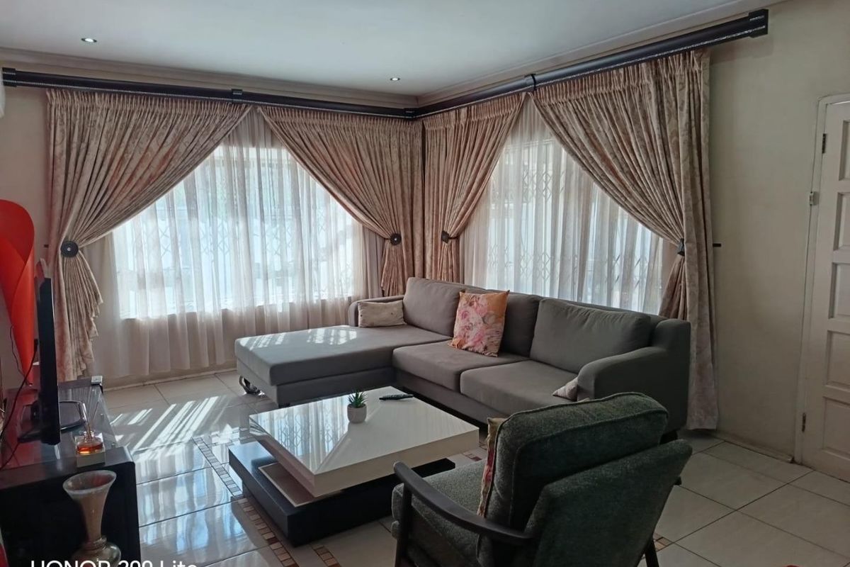 A comfortable living room featuring tiled flooring, recessed downlighting, and large windows dressed with floor-to-ceiling curtains.