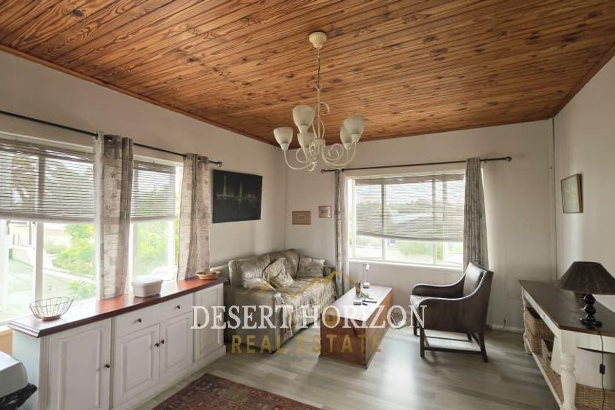 A cozy living room featuring a distinctive timber-clad ceiling, built-in cabinetry, and large windows that provide ample natural light.