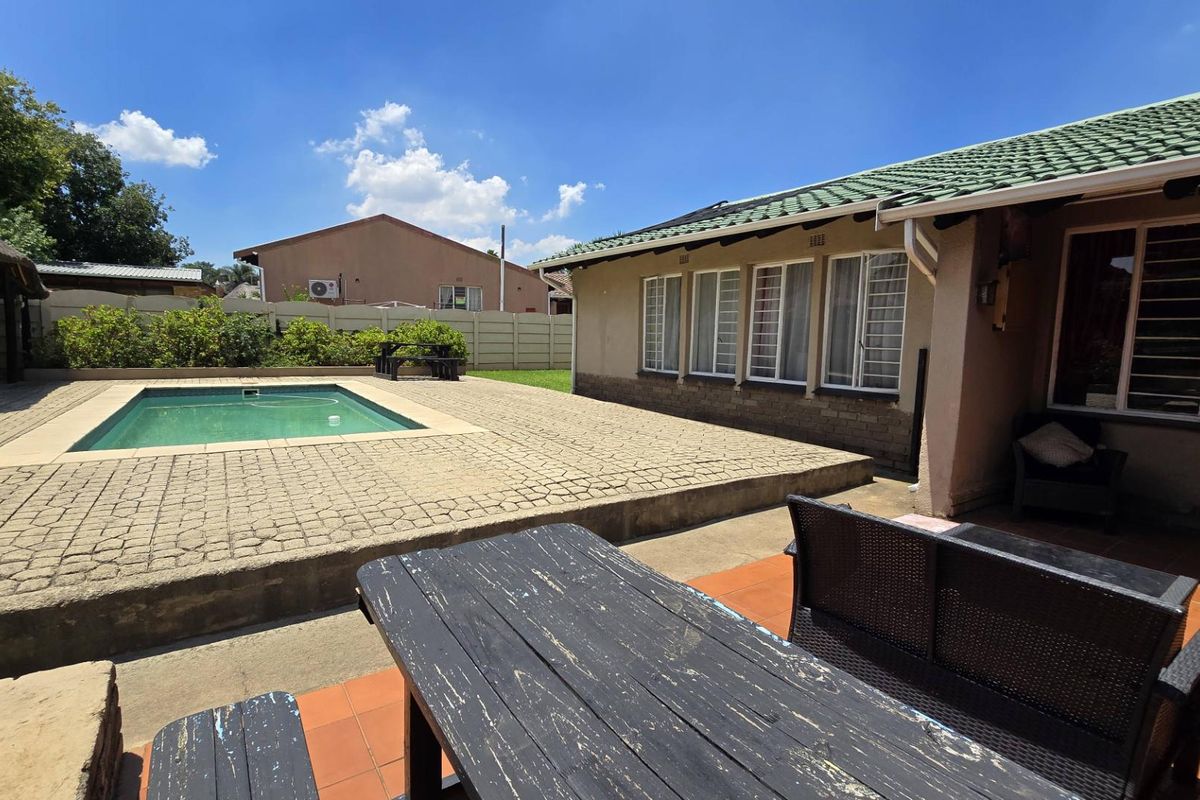 Rear exterior view featuring a swimming pool, paved patio area, and a covered outdoor space with tiled flooring.