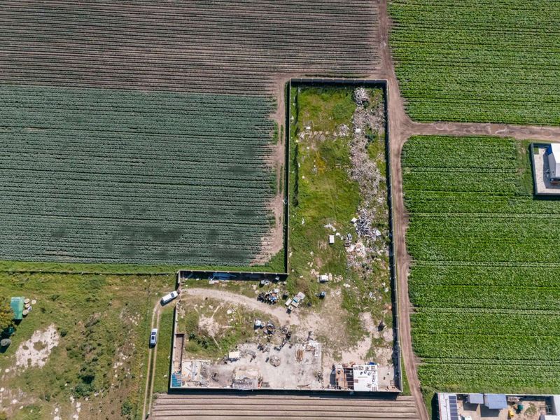 Aerial view of a vacant residential plot enclosed by a perimeter wall, featuring cleared ground and existing concrete foundation remnants.