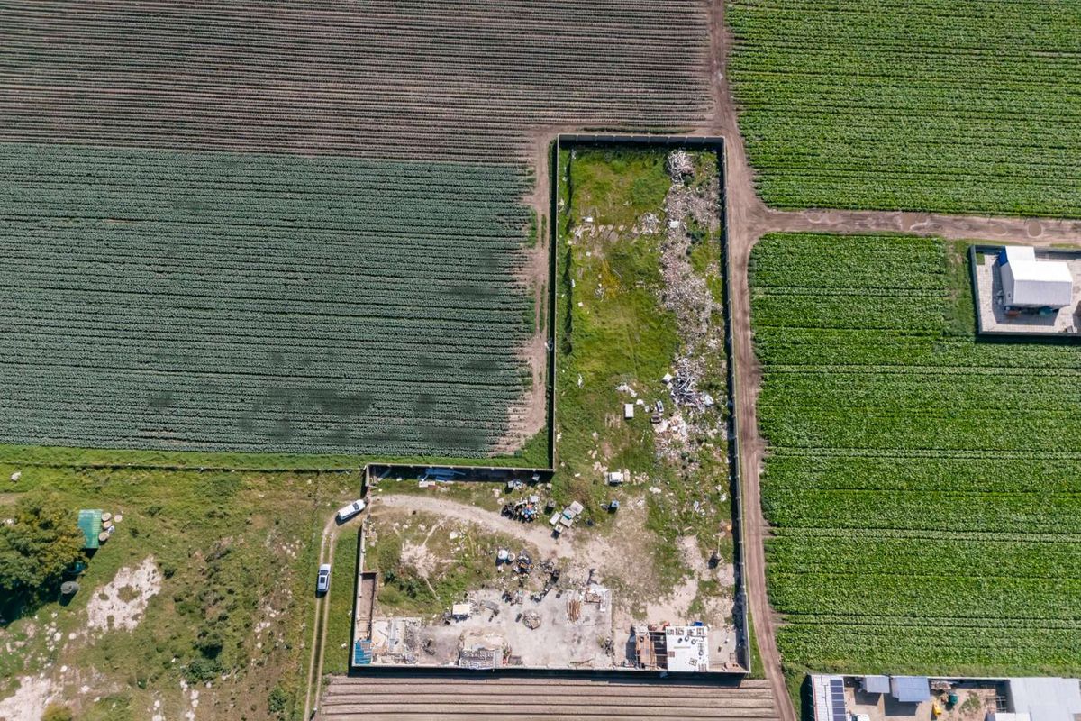 Aerial view of a vacant residential plot enclosed by a perimeter wall, featuring cleared ground and existing concrete foundation remnants.