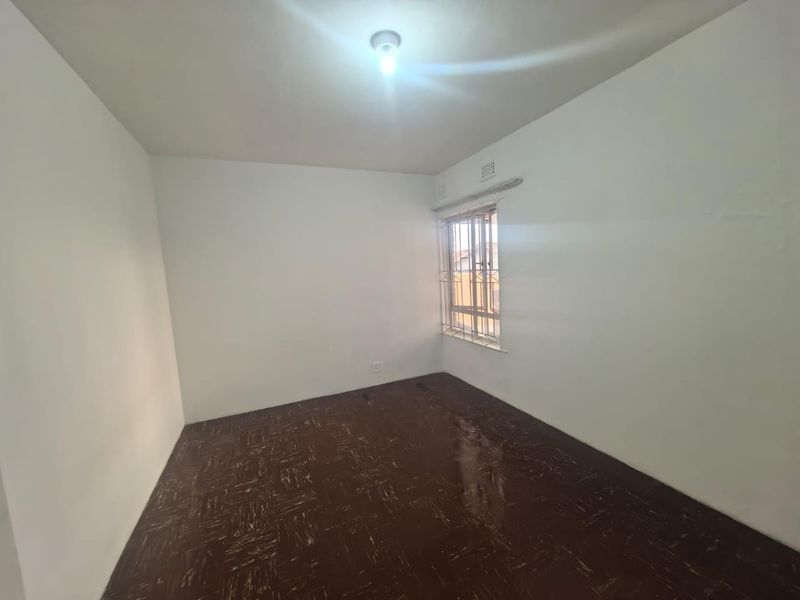 An empty bedroom featuring original parquet flooring and a window fitted with security bars, offering a blank canvas for renovation.