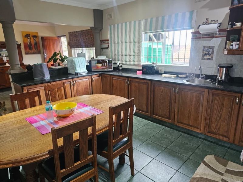 Open-plan kitchen and dining area featuring wooden cabinetry, granite countertops, and ceramic tiled flooring with a functional layout.