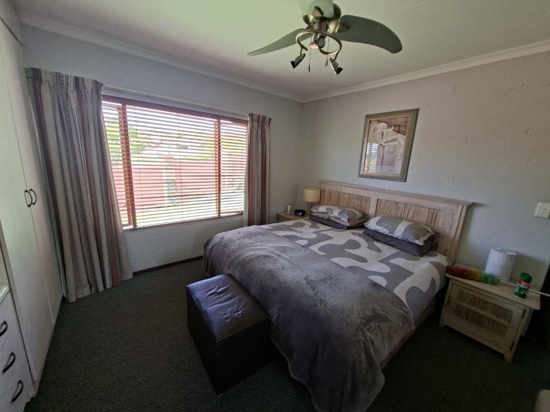A functional bedroom featuring built-in cupboards, a ceiling fan, and venetian blinds, offering a comfortable and practical living space.