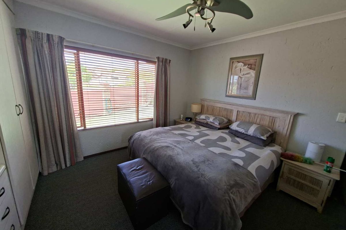 A functional bedroom featuring built-in cupboards, a ceiling fan, and venetian blinds, offering a comfortable and practical living space.