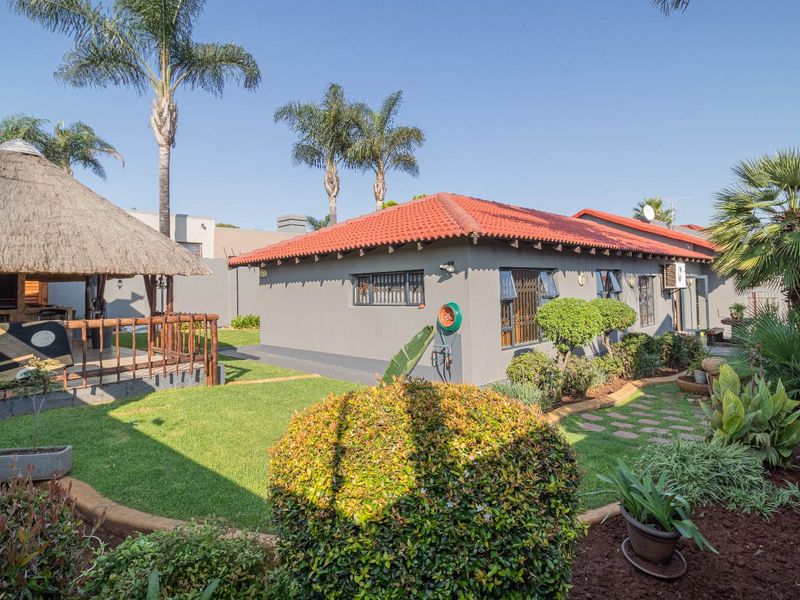 A well-maintained rear garden featuring a thatched lapa, paved pathways, and a neat lawn area adjacent to the main dwelling with a tiled roof.