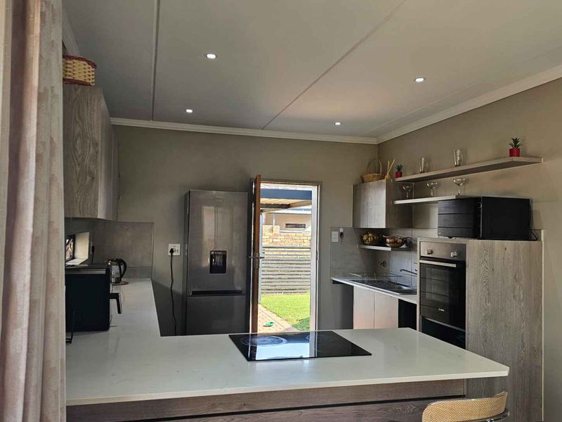 Modern kitchen featuring sleek built-in cabinetry, stone countertops, integrated electric hob, built-in oven, and recessed lighting, with direct access to the rear garden.