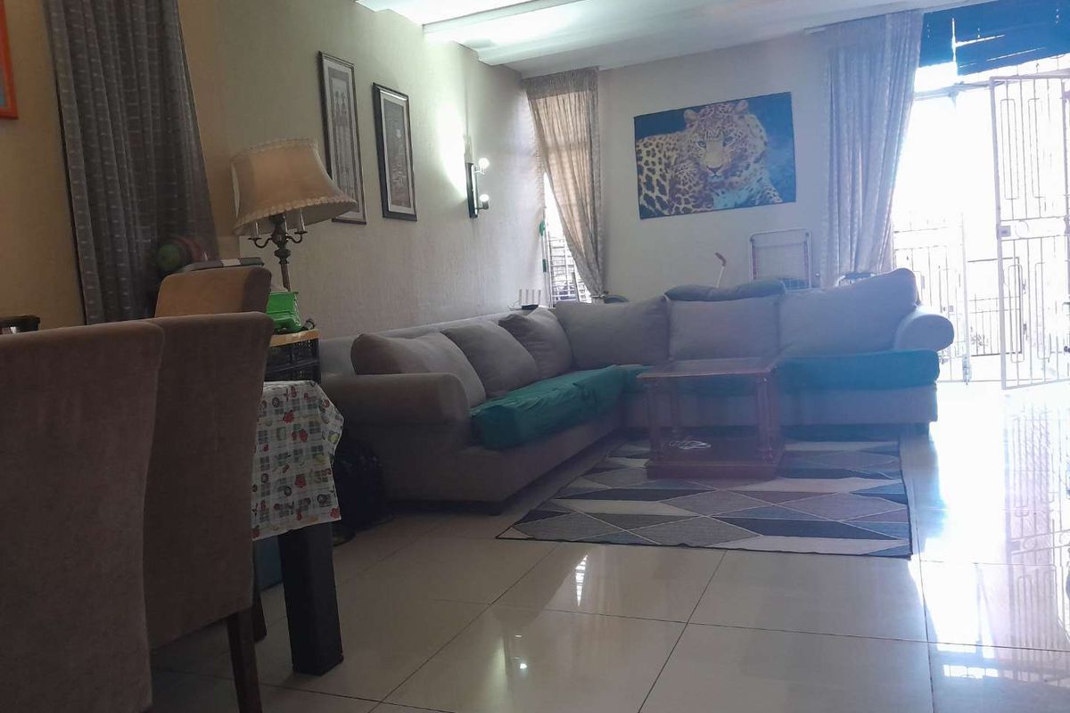 A living room area featuring tiled flooring and access to an exterior space through a security gate and sliding door.