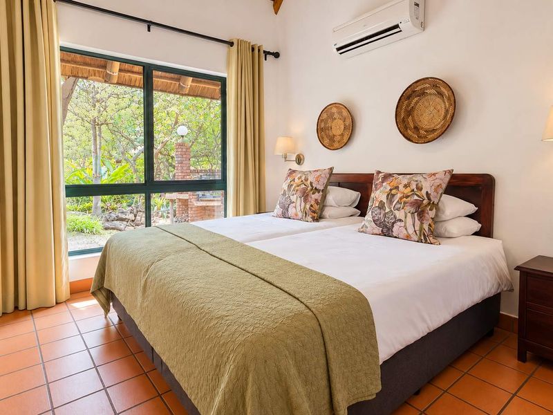 A well-maintained bedroom featuring tiled flooring, an air conditioning unit, and large windows providing a view of the outdoor garden area.