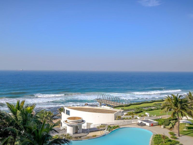 Stunning elevated ocean view overlooking a swimming pool, manicured gardens, and the coastal promenade.