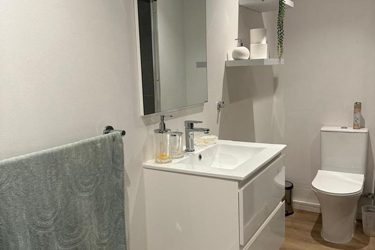 A modern bathroom featuring a wall-mounted vanity with basin, a sleek mirror, and a contemporary toilet, finished with wood-look flooring and recessed lighting.