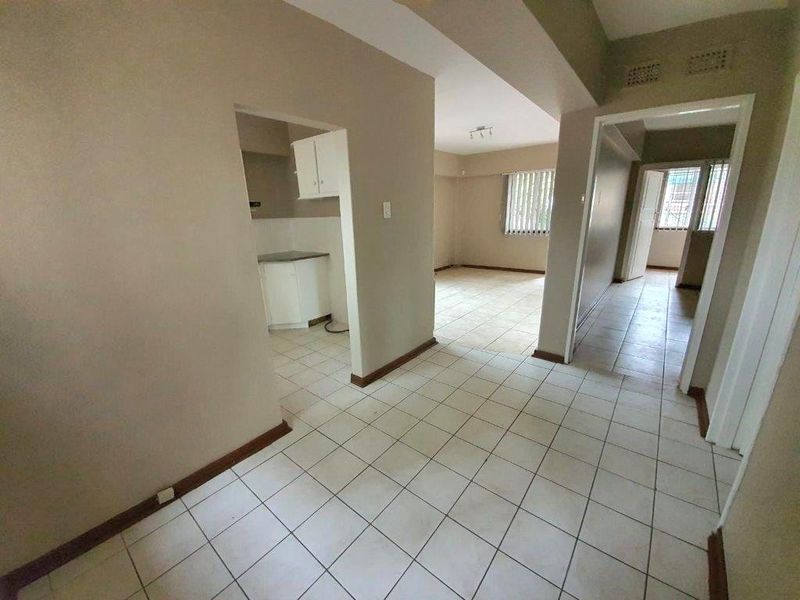 An open-plan living and kitchen area featuring neutral wall tones and tiled flooring throughout, presenting a blank canvas for potential interior updates.