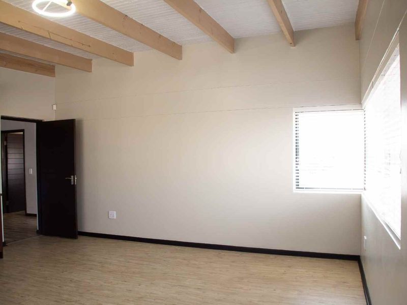 A bright, empty living room featuring exposed timber ceiling beams, light-toned laminate flooring, and neutral walls, offering a clean and versatile living space.