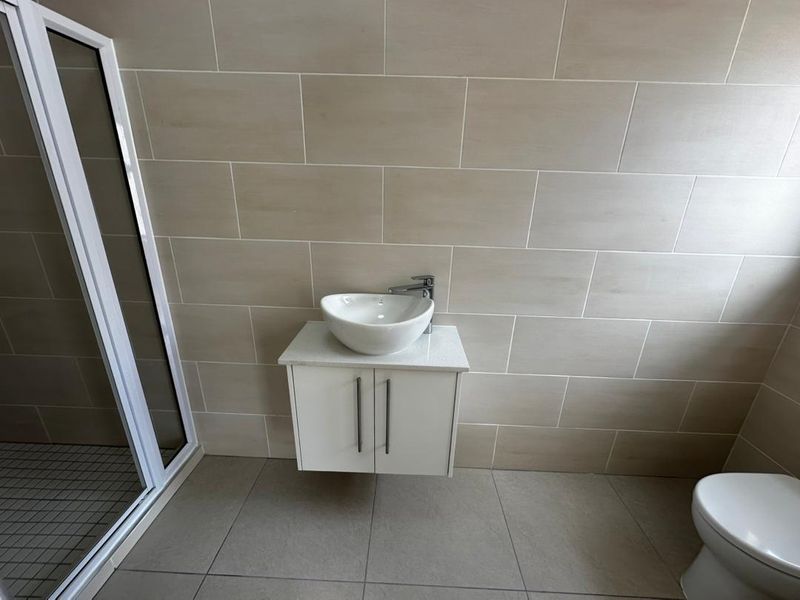 A modern bathroom featuring a wall-mounted vanity with a vessel sink, a glass shower enclosure, and neutral ceramic tiling throughout.