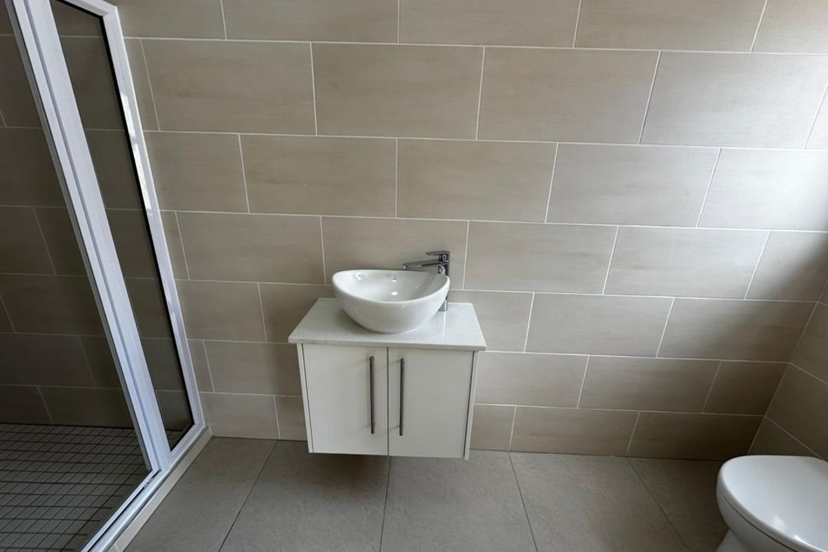 A modern bathroom featuring a wall-mounted vanity with a vessel sink, a glass shower enclosure, and neutral ceramic tiling throughout.