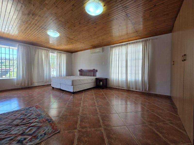 Spacious bedroom featuring a timber tongue and groove ceiling, tiled flooring, built-in cupboards, and a wall-mounted air conditioning unit.
