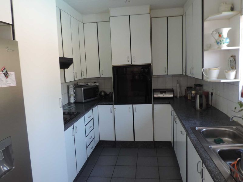 A functional U-shaped kitchen featuring white cabinetry, dark laminate countertops, built-in oven, extractor fan, and a stainless steel double sink.